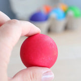 Adult hand holding a red Grimms rainbow ball showing size