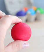 Adult hand holding a red Grimms rainbow ball showing size