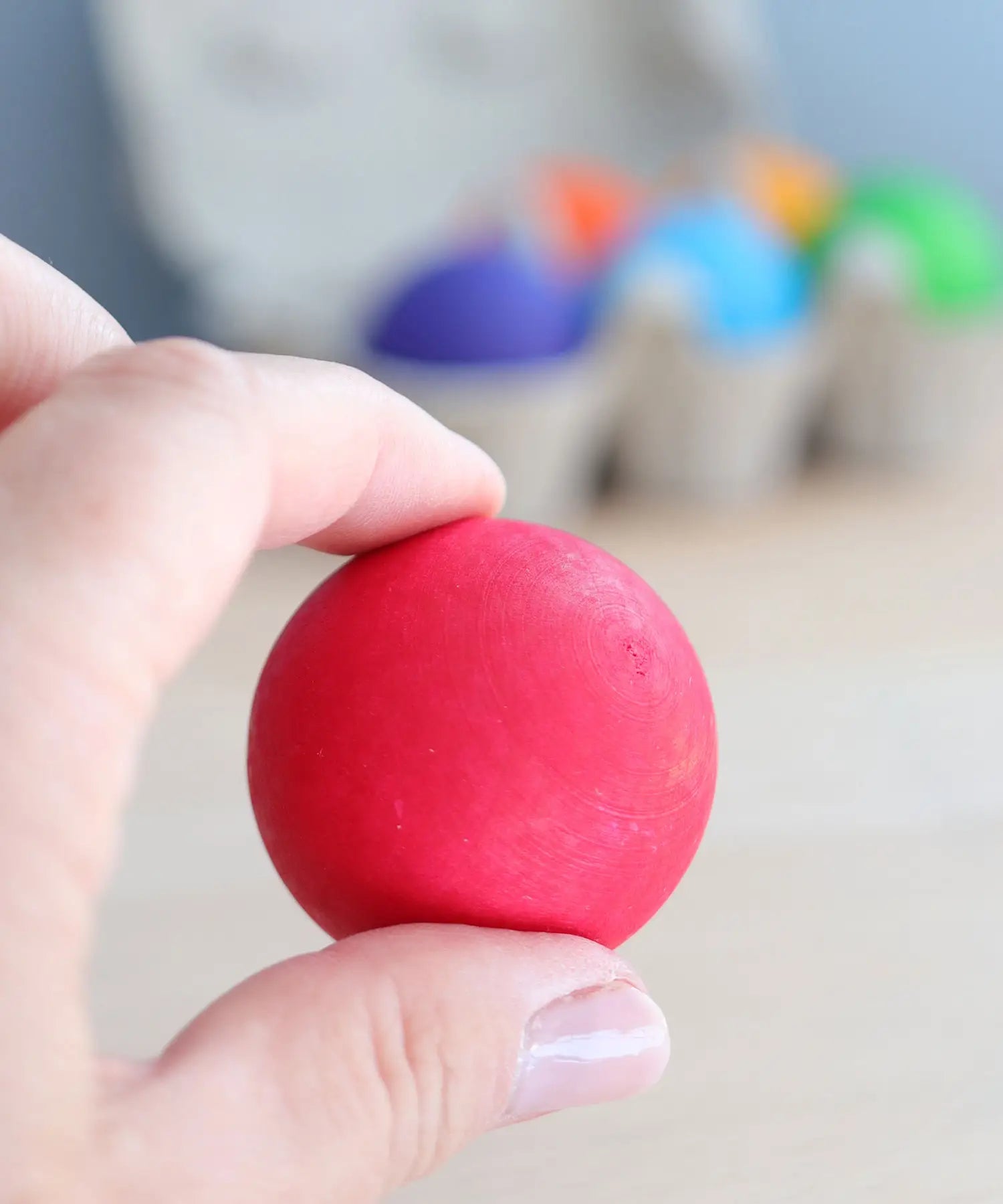 Adult hand holding a red Grimms rainbow ball showing size
