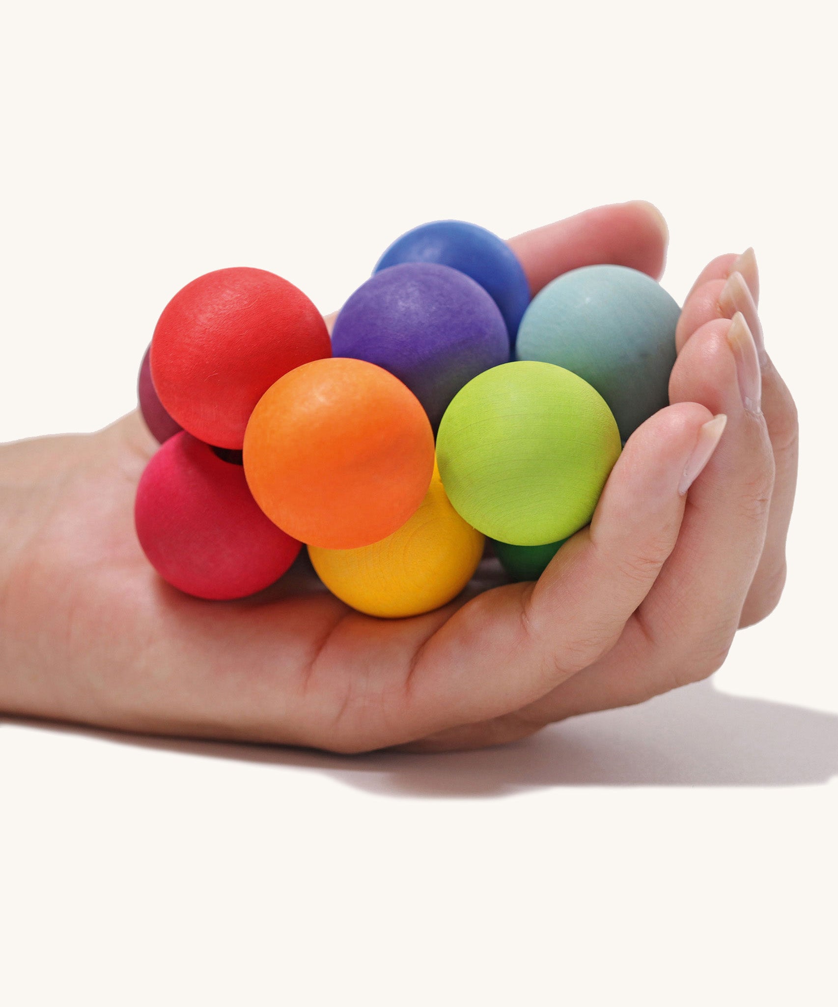 The Grimm's Rainbow Beads Grasper toy shown in an adult's hand. 