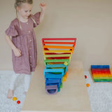 Child rolling a Grimms wooden rainbow ball down a ball run made from rainbow boards