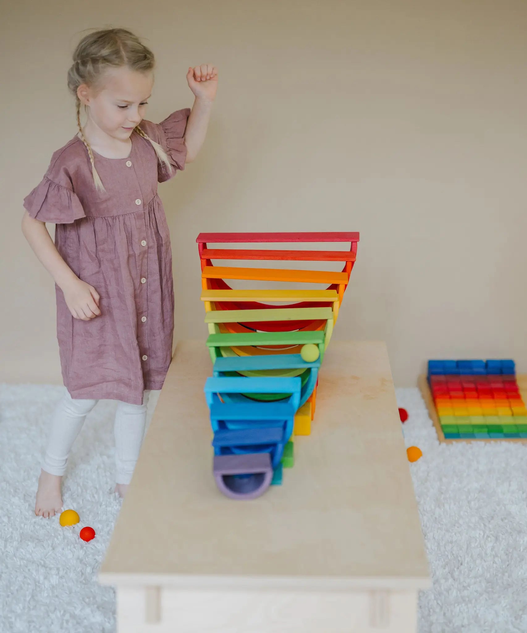 Child rolling a Grimms wooden rainbow ball down a ball run made from rainbow boards