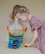 Child looking down at a ball run made from Grimms wooden rainbow pieces 