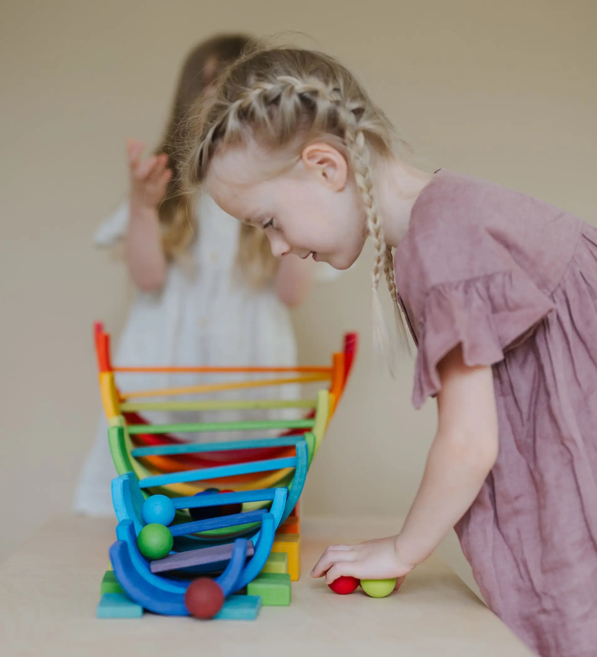 Child looking down at a ball run made from Grimms wooden rainbow pieces 