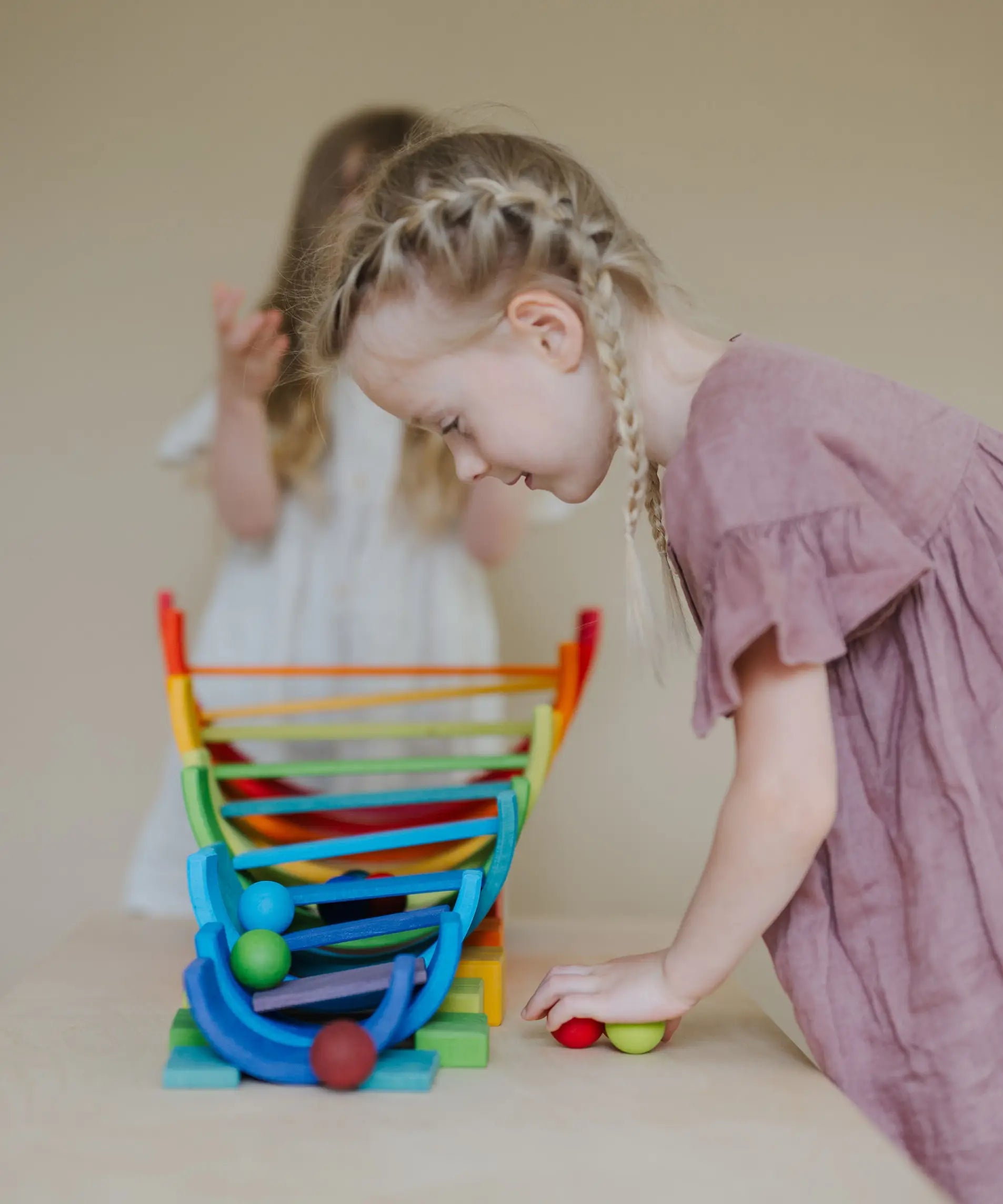 Child looking down at a ball run made from Grimms wooden rainbow pieces 