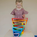 Child standing behind a ball run made from Grimms wooden rainbow boards, and other blocks