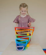 Child standing behind a ball run made from Grimms wooden rainbow boards, and other blocks