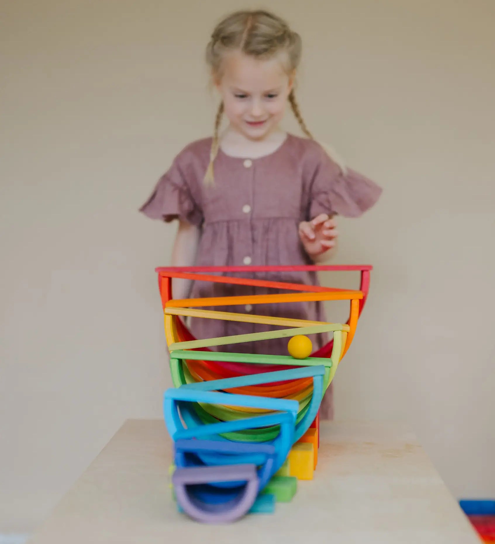 Child standing behind a ball run made from Grimms wooden rainbow boards, and other blocks
