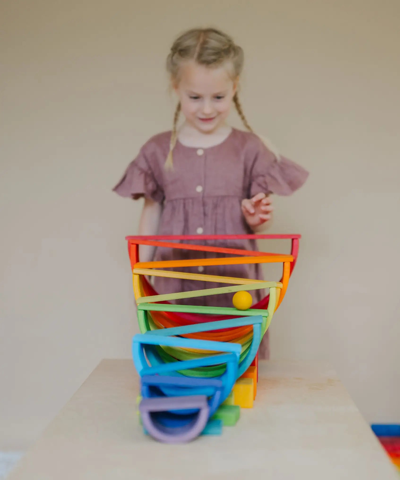 Child standing behind a ball run made from Grimms wooden rainbow boards, and other blocks
