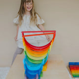 Child standing behind a structure made from Grimms wooden rainbow building boards and other building blocks
