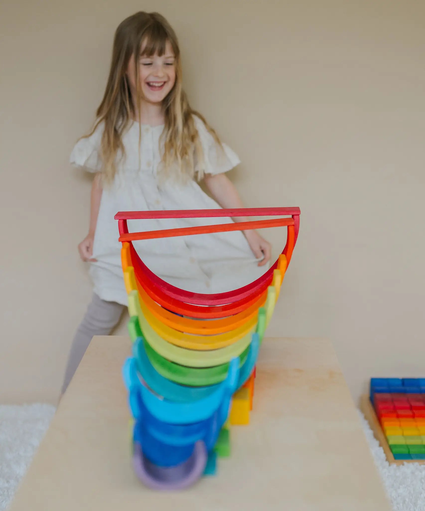 Child standing behind a structure made from Grimms wooden rainbow building boards and other building blocks