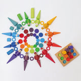 Grimms wooden coins in a pattern with other loose pieces next to a sorting board in a rainbow palette