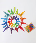 Grimms wooden coins in a pattern with other loose pieces next to a sorting board in a rainbow palette