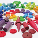 A flat lay made from Grimms wooden peg dolls, rings, coins and other loose pieces in a rainbow palette