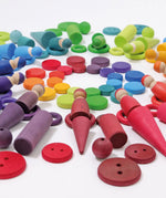 A flat lay made from Grimms wooden peg dolls, rings, coins and other loose pieces in a rainbow palette