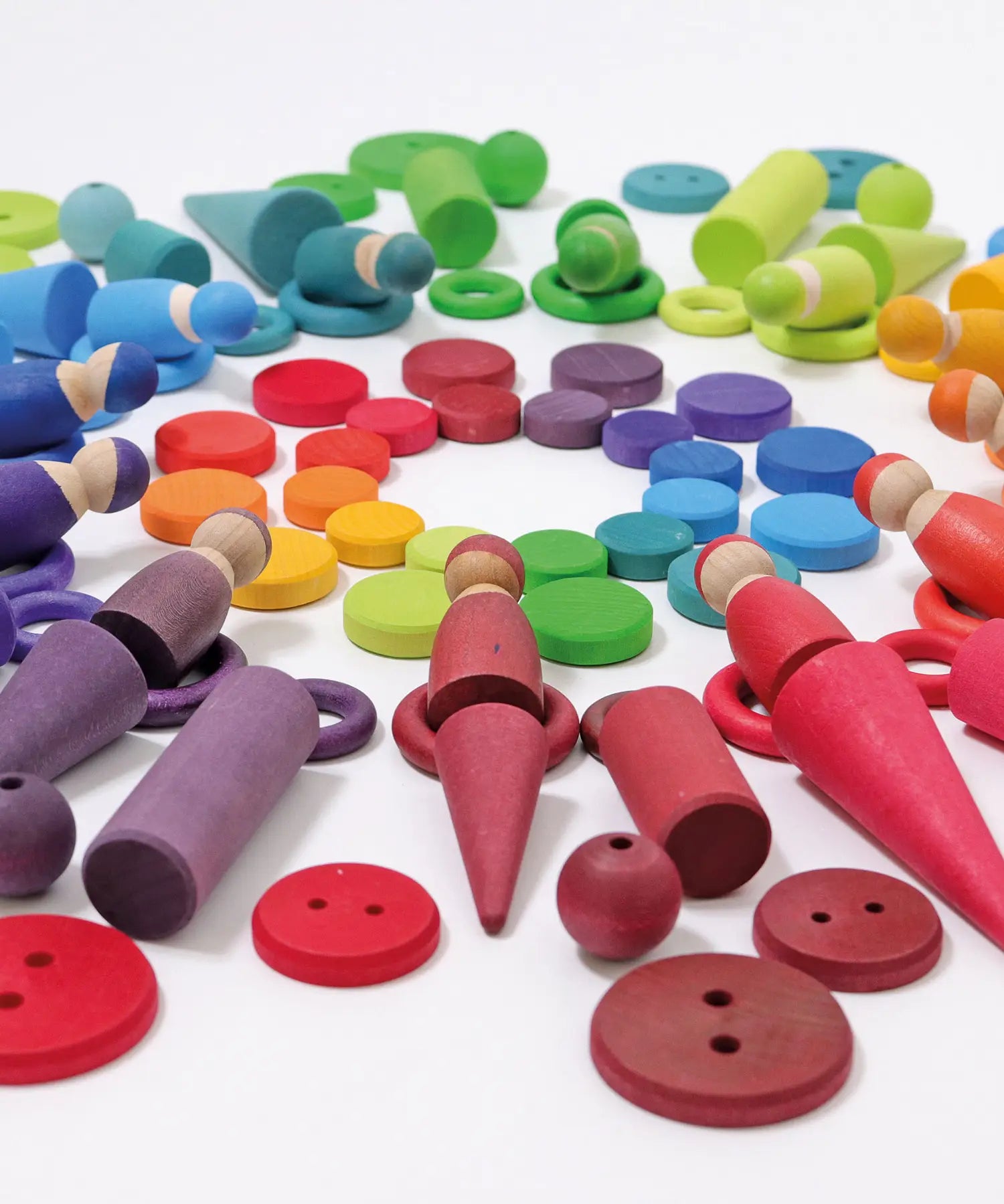 A flat lay made from Grimms wooden peg dolls, rings, coins and other loose pieces in a rainbow palette
