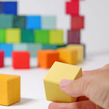 Adult hand holding a yellow Grimms wooden cube block showing scale.