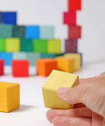 Adult hand holding a yellow Grimms wooden cube block showing scale.