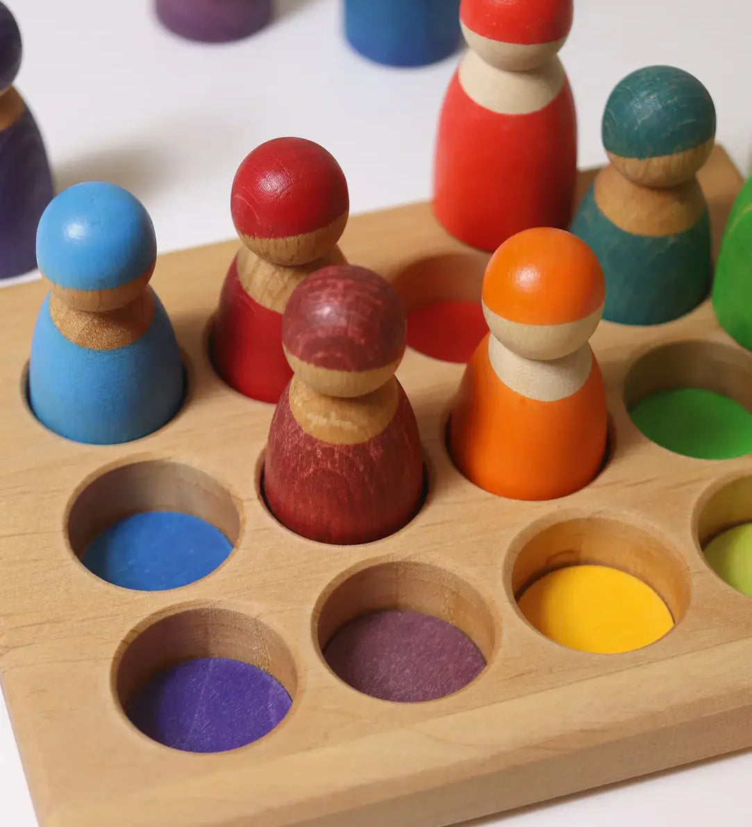 Grimms handcrafted sorting board with rainbow coloured peg dolls sitting inside the round slots 