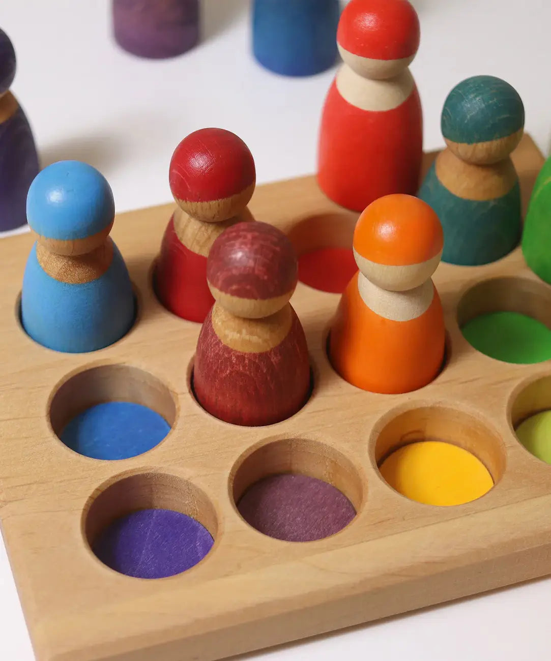 Grimms handcrafted sorting board with rainbow coloured peg dolls sitting inside the round slots 
