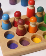 Grimms handcrafted sorting board with rainbow coloured peg dolls sitting inside the round slots 