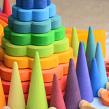 Grimms wooden forest pieces in a rainbow palette in front of a flower shaped stacking toy