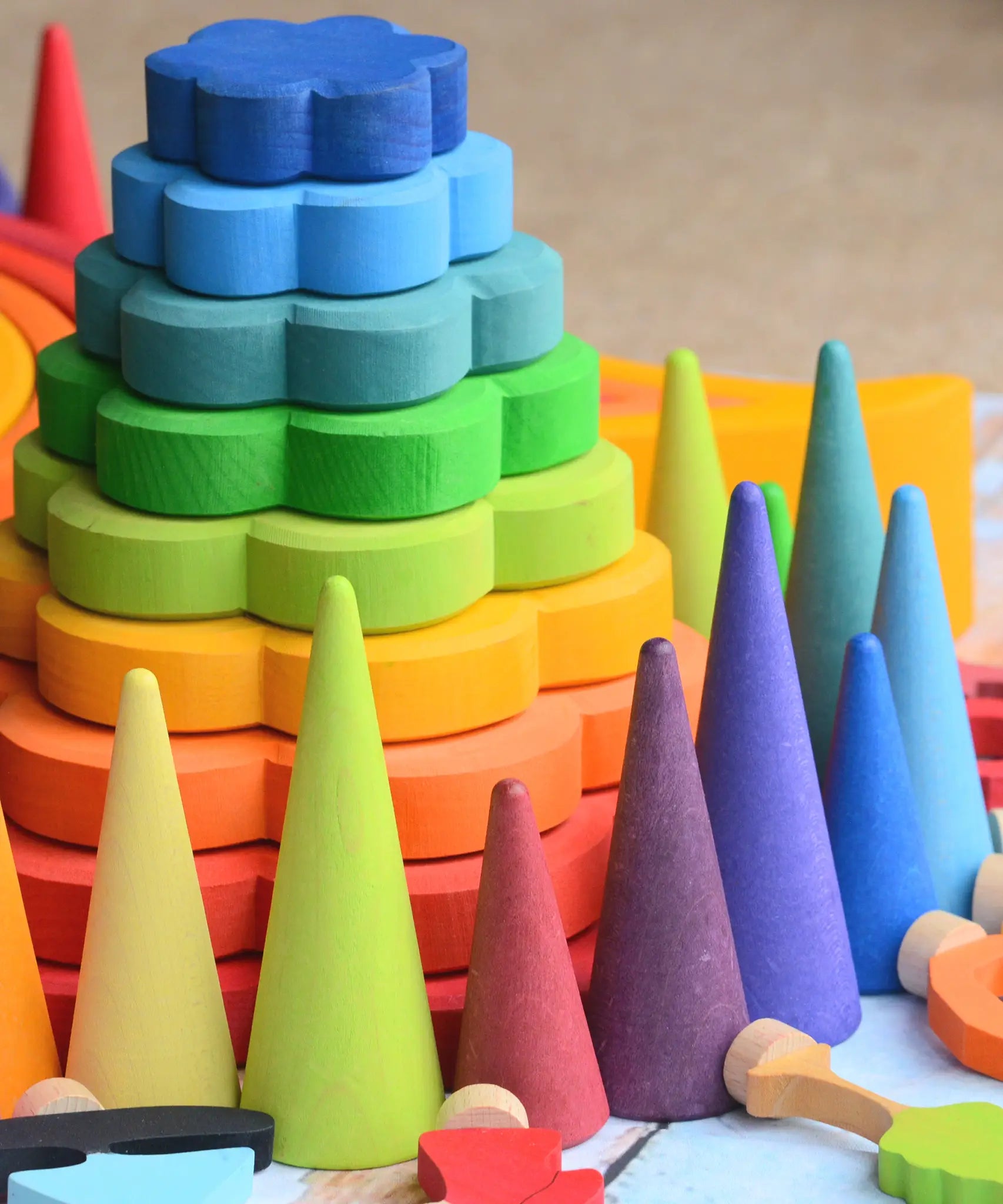 Grimms wooden forest pieces in a rainbow palette in front of a flower shaped stacking toy