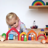 Child playing with the Grimms wooden house set in a rainbow palette with other matching blocks and peg dolls