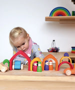 Child playing with the Grimms wooden house set in a rainbow palette with other matching blocks and peg dolls