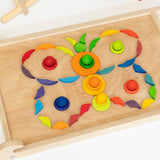 A butterfly flatlay made from Grimms hand crafted wooden loose pieces including balls, rings, disks on. a Triclimb Biri board