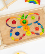 A butterfly flatlay made from Grimms hand crafted wooden loose pieces including balls, rings, disks on. a Triclimb Biri board