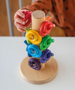 Child sorting loose Grimms wooden rings in a rainbow palette on a sorting helper. 