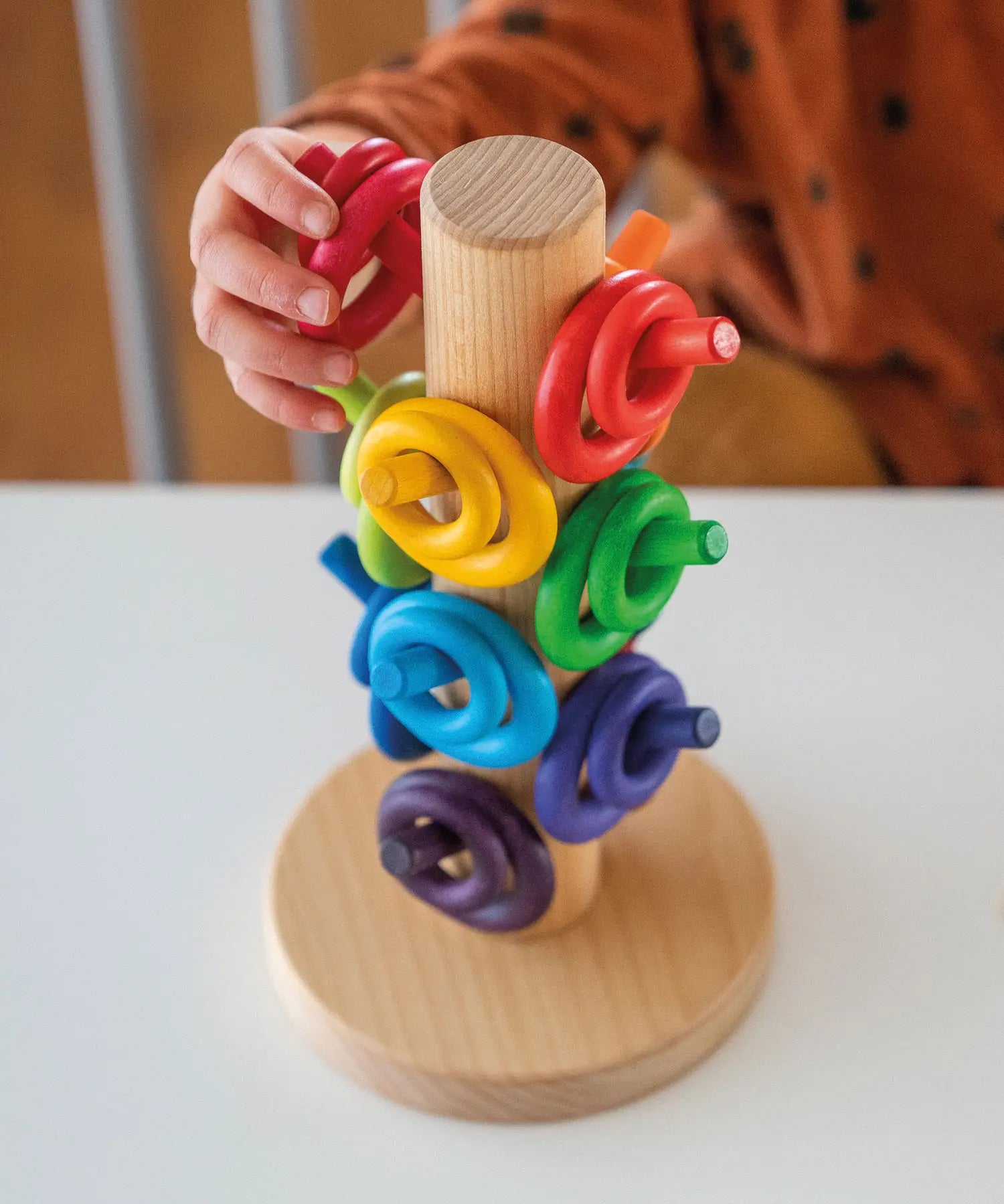 Child sorting loose Grimms wooden rings in a rainbow palette on a sorting helper. 