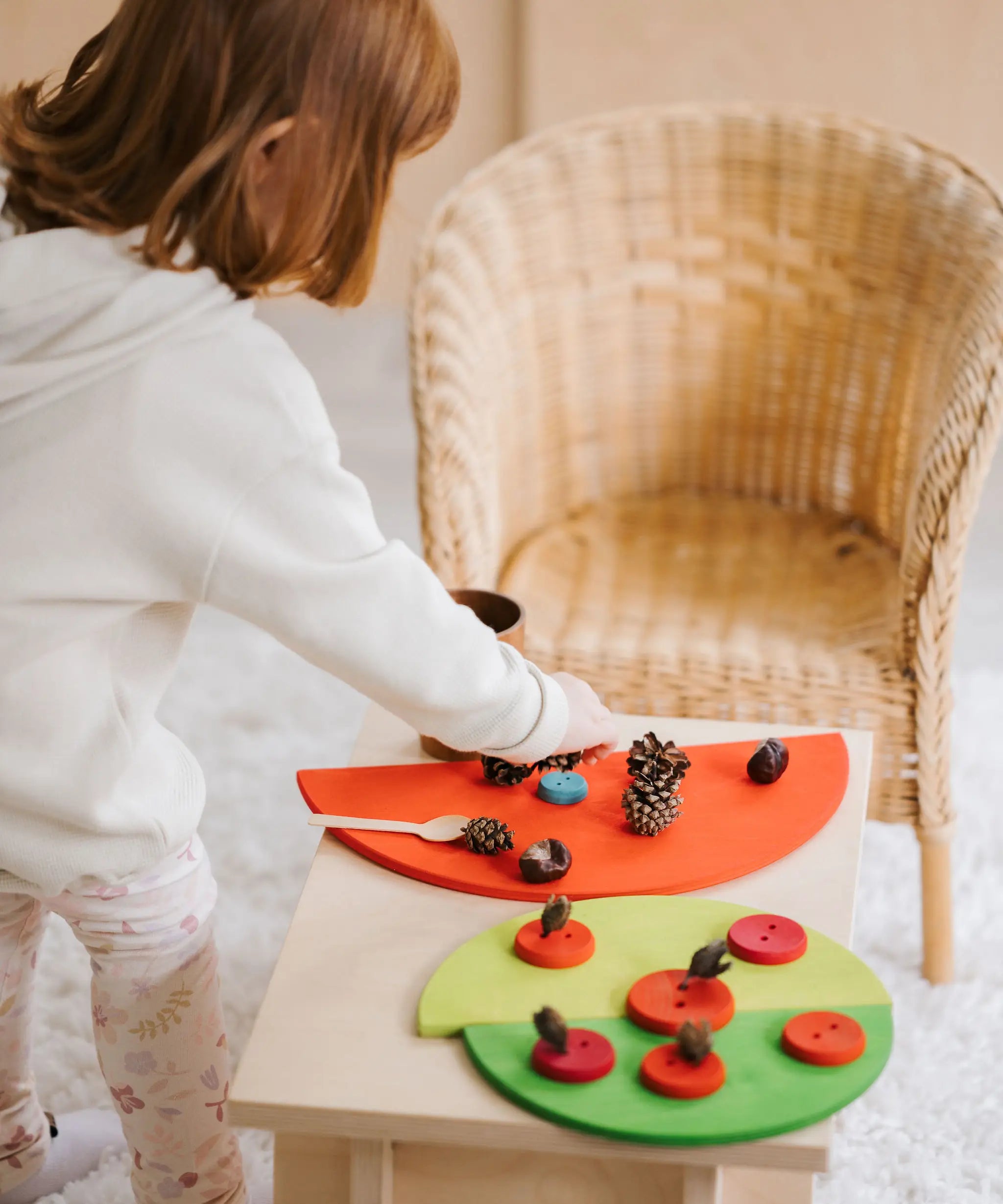 Child playing a sorting game using Grimms wooden semi circles, buttons and pine cones. 