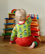 Child sitting next to a stack made from Grimms wooden rainbow semi circle and natural arch pieces