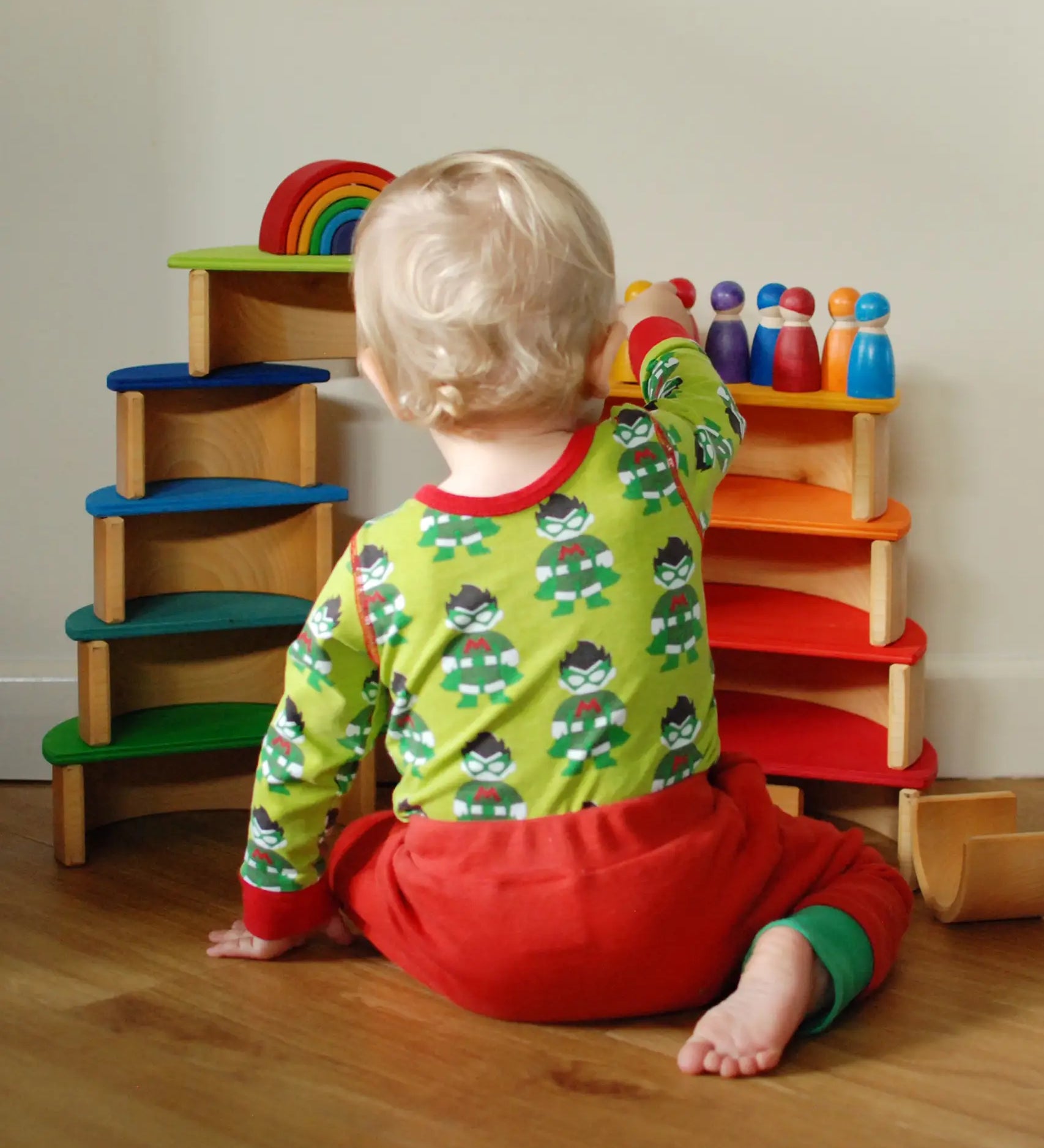 Child sitting next to a stack made from Grimms wooden rainbow semi circle and natural arch pieces