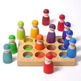 Grimms handcrafted wooden sorting board showing rainbow coloured peg dolls sitting on the slots