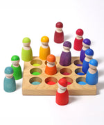 Grimms handcrafted wooden sorting board showing rainbow coloured peg dolls sitting on the slots