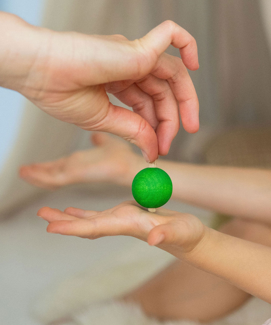 An adult's hand placing a green coloured rainbow spinning top on another child's hand. These Grimm's toys are part of a wide range of wooden toys available here at Babipur. 
