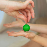 An adult's hand placing a green coloured rainbow spinning top on another child's hand. These Grimm's toys are part of a wide range of wooden toys available here at Babipur. 