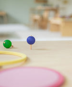 A green and purple coloured rainbow spinning tops in motion on a wooden surafce. These Grimm's toys are part of a wide range of wooden toys available here at Babipur. 