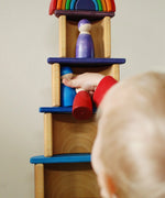 Child placing small peg dolls on a stack made using Grimms bright rainbow semi  circles