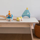 Grimm's wooden stacking car toys placed on a wooden table with a Grimm;s friend peg doll on top of them. These Grimm's toys are part of a wide range of wooden toys available here at Babipur. 