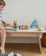 A child playing with the Grimm's wooden stacking car toys placed on a wooden table with a Grimm's friend peg doll on top of them. These Grimm's toys are part of a wide range of wooden toys available here at Babipur. 