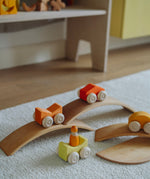 Orange Grimm's wooden stacking cars toys placed on Grimm's bridge pieces. These Grimm's toys are part of a wide range of wooden toys available here at Babipur. 