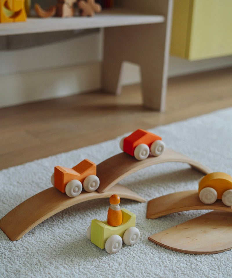 Orange Grimm's wooden stacking cars toys placed on Grimm's bridge pieces. These Grimm's toys are part of a wide range of wooden toys available here at Babipur. 