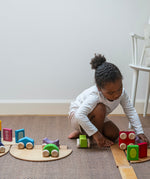 A child playing with the Grimm's wooden stacking car toys driving them over a Grimm's bridge piece. These Grimm's toys are part of a wide range of wooden toys available here at Babipur. 