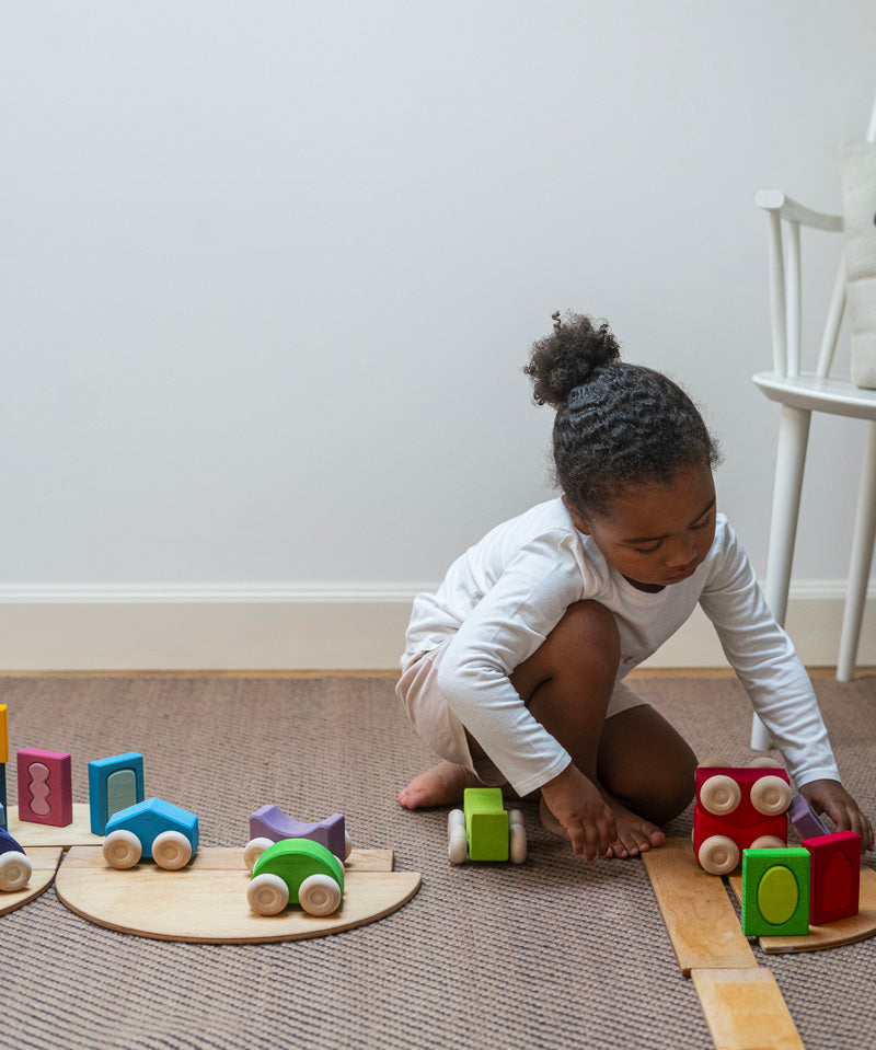 A child playing with the Grimm's wooden stacking car toys driving them over a Grimm's bridge piece. These Grimm's toys are part of a wide range of wooden toys available here at Babipur. 