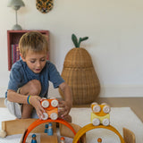 A child playing with the orange Grimm's wooden stacking car toys placing them on a Grimm's bridge piece. These Grimm's toys are part of a wide range of wooden toys available here at Babipur. 