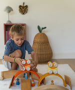 A child playing with the orange Grimm's wooden stacking car toys placing them on a Grimm's bridge piece. These Grimm's toys are part of a wide range of wooden toys available here at Babipur. 